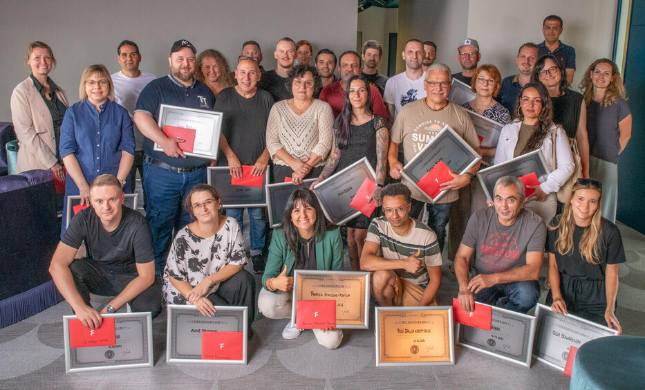 Gruppe von Mitarbeitenden mit Urkunden, Diplomen und Auszeichnungen auf Gruppenfoto.